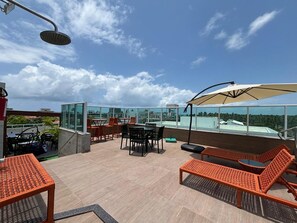 Terraço no telhado com área de estar externa, mesa e um guarda-sol grande.