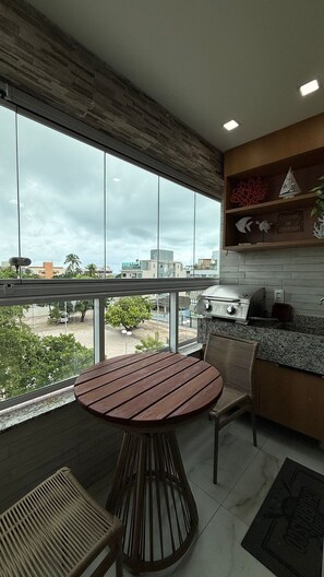 A modern kitchen with a round table and chairs, a view of the city, and a balcony with a railing. - TNP - Makaranduba 301 (Ipojuca)