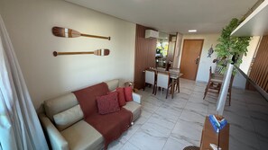 Uma sala de estar com sofá, uma mesa de jantar com cadeiras e uma escada para outro andar.