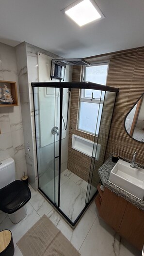 Casa de banho moderna com chuveiro em cabine de vidro, toucador com lavatório e espelho.