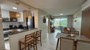 A modern kitchen with a central island, dining area with a table and chairs, and a view of the outdoors. - TNP - Makaranduba 301 (Ipojuca)