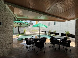 Un patio al aire libre con piscina, mesa y sillas, y sombrillas.