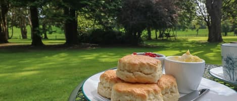 Ein Tisch mit Keksen, Marmelade, einer Tasse Tee und einem Messer in einem Park.