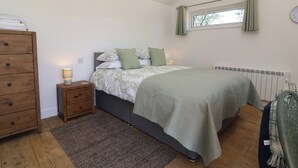 A bedroom with a bed, a nightstand, a dresser, a window with curtains, and a radiator. - Willow (Barnstaple)