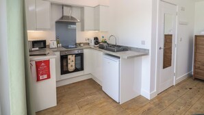 Una cuina compacta amb armaris blancs, forn integrat, microones, cafetera i rentatge.