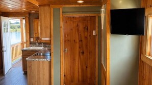 Interior d'una cabana de fusta amb zona de cuina, una porta i una televisió penjada a la paret.