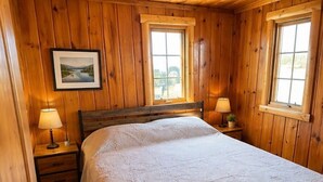Una habitació amb panells de fusta, un llit, dues làmpades de nit, un quadre a la paret i dues finestres.