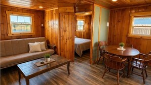 Interior d'una cabana de fusta amb un sofà, taula de dinar, cadires i un llit.