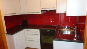 Une cuisine de taille réduite avec des meubles blancs, une cuisinière noire et un pare-feu rouge.