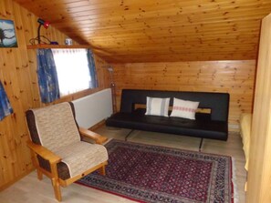 Una habitació acollidora amb un sostre de fusta, un sofà, una cadira i una catifes amb dibuixos.