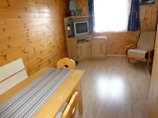 A wooden cabin interior with a bed, a TV, a chair, and a table.