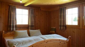 Ein Zimmer in einer Holzhütte mit einem Bett, zwei Fenstern und einer Deckenleuchte.