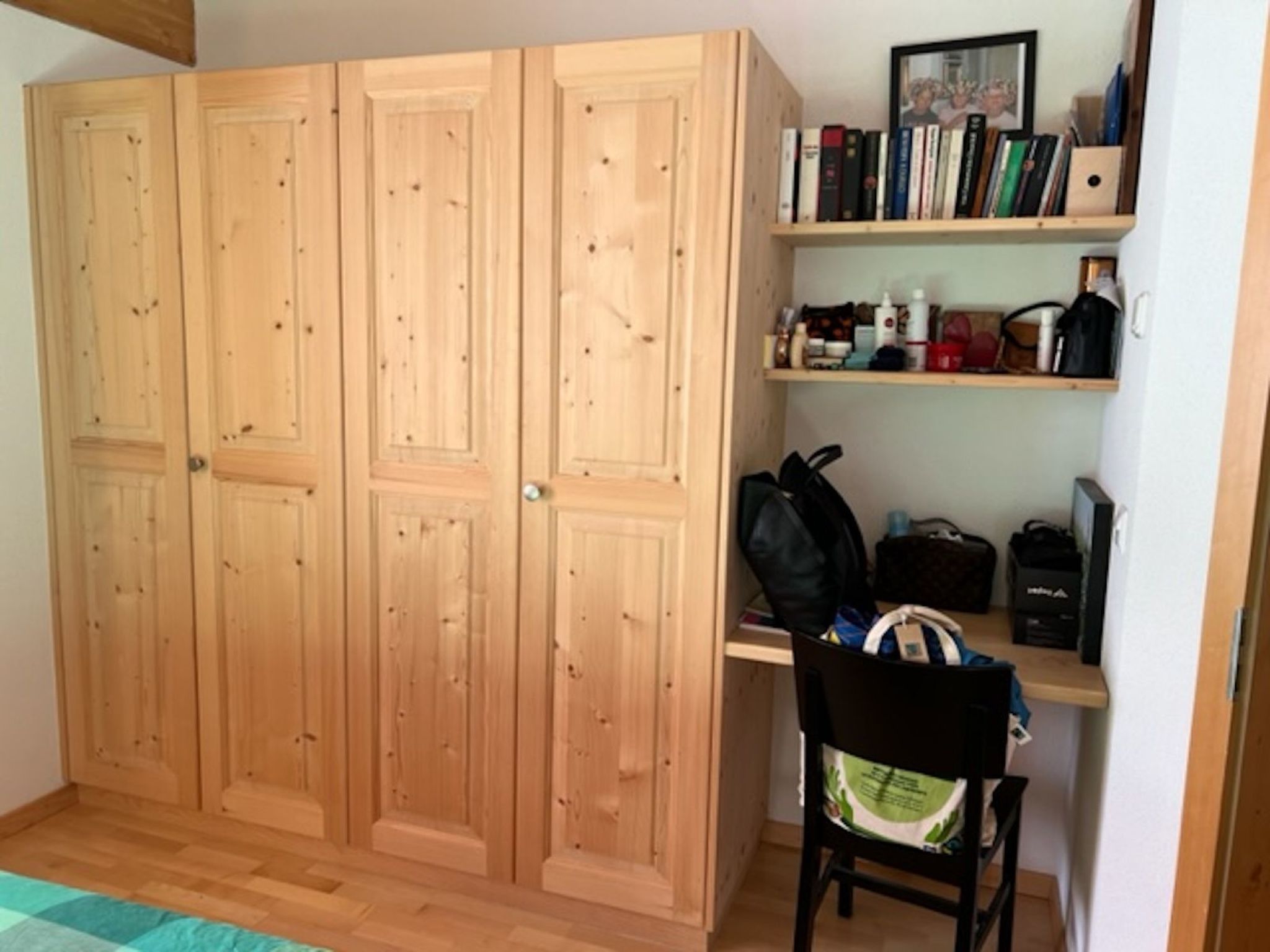 Una habitación con un armario de madera, un escritorio con silla y una estantería con libros y objetos personales.