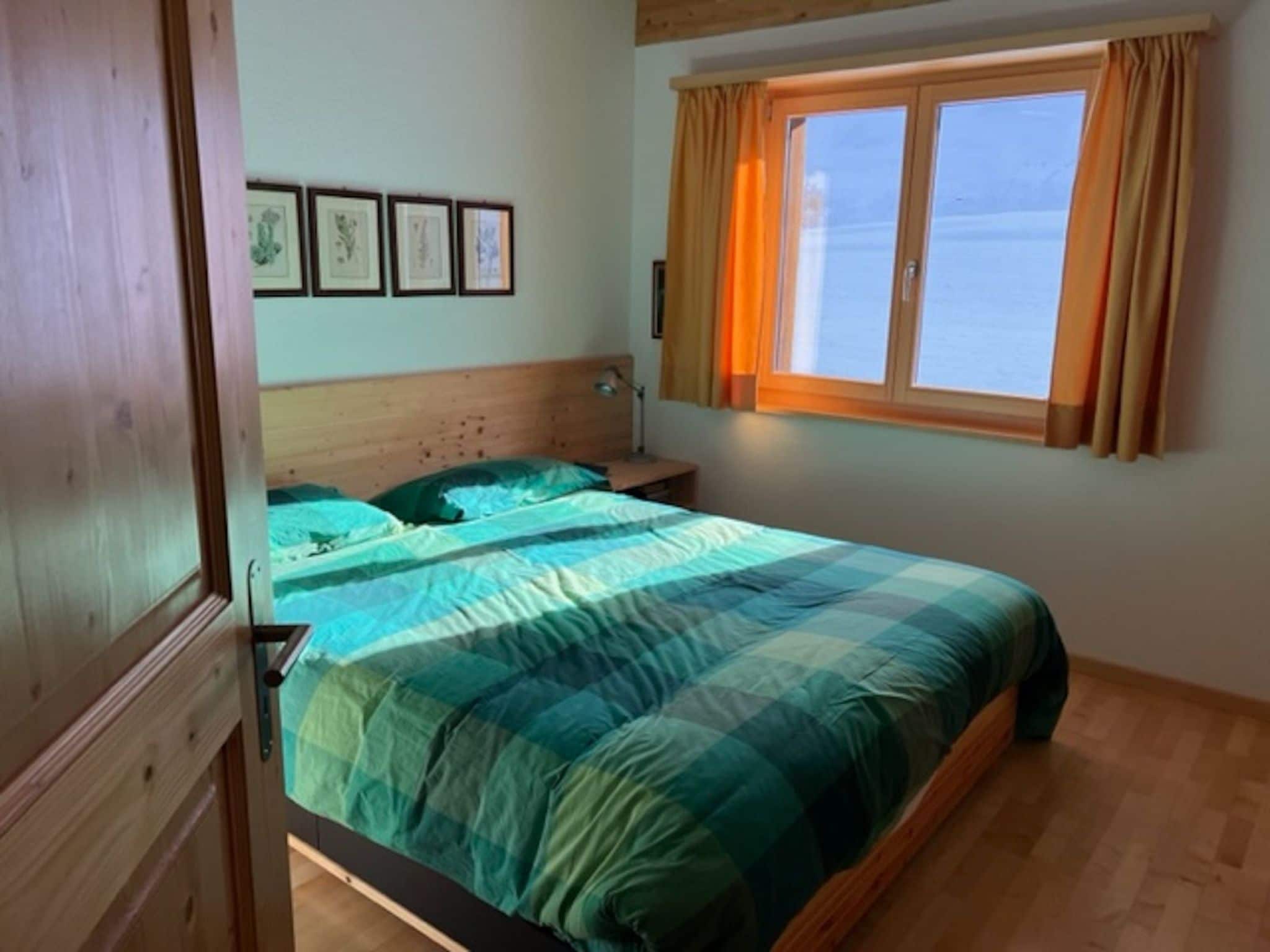 Ein Schlafzimmer mit einem Bett, einem Nachttisch, einem Fenster mit Vorhängen und gerahmten Bildern an der Wand.