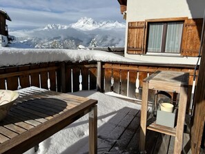 A wooden deck with a table and a small table, overlooking a snowy mountain landscape. - Alpatli, Obersaxen-Miraniga, (Obersaxen), 38095B by Interhome (Obersaxen Affeier)