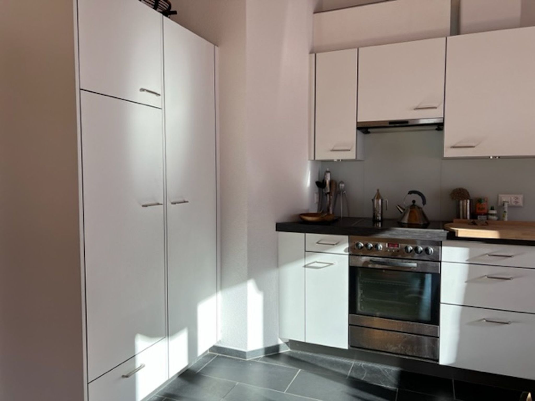 Una cocina moderna con armarios blancos, horno de acero inoxidable y encimera negra.