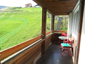 A wooden balcony with a view of a green hillside, a set of stairs leading down, and two red chairs with green cushions. - Casa Crestas 147, Vignogn, (Vignogn), 47000B by Interhome (Vignogn)