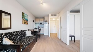 A compact living space with a sofa, a dining table, a kitchen area with a microwave and refrigerator, and a hallway leading to another room. - Bright flat for 4 people, right next to the shops (Grasse)