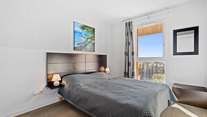 A bedroom with a bed, bedside lamps, a window with curtains, and a painting on the wall. - Bright flat for 4 people, right next to the shops (Grasse)