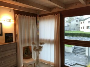 A room with a wooden ceiling, a window with curtains, a chair, a small table, and a vase with dried flowers. - Ferienhaus Carrera mit Traumgarten, Valendas, (Valendas), 22007B by Interhome (Valendas)