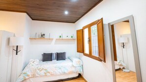 Un dormitorio con cama, techo de madera, ventana con contraventanas de madera y espejo.