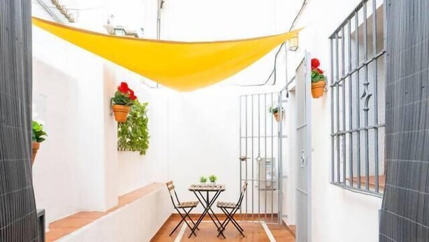 Un patio estrecho con suelo de baldosas, una mesa con sillas y plantas en macetas.