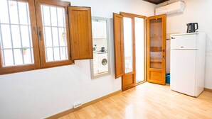 Una habitación con suelo de madera, un refrigerador blanco, una lavadora y una ventana con contraventanas de madera.