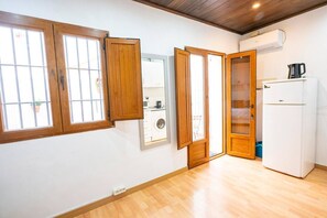 Ein Zimmer mit Holzboden, einem weißen Kühlschrank, einer Waschmaschine und einem Fenster mit Holzläden.