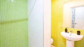 Un baño con paredes de azulejos verdes y amarillos, un lavamanos blanco y un espejo.