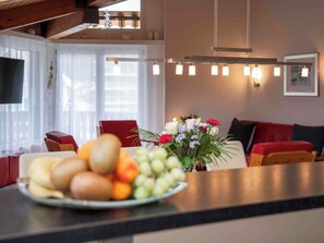 Ein modernes Wohnzimmer mit Essbereich, mit Holzboden, Flachbildfernseher, einer Pendelleuchte und einer Obstschale auf der Arbeitsplatte.