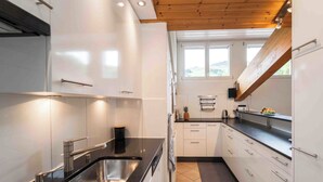 A modern kitchen with white cabinets, a black countertop, and a wooden ceiling. - Arnika Attika, Obersaxen Affeier, (Obersaxen Affeier), 34105B by Interhome (Obersaxen Affeier)