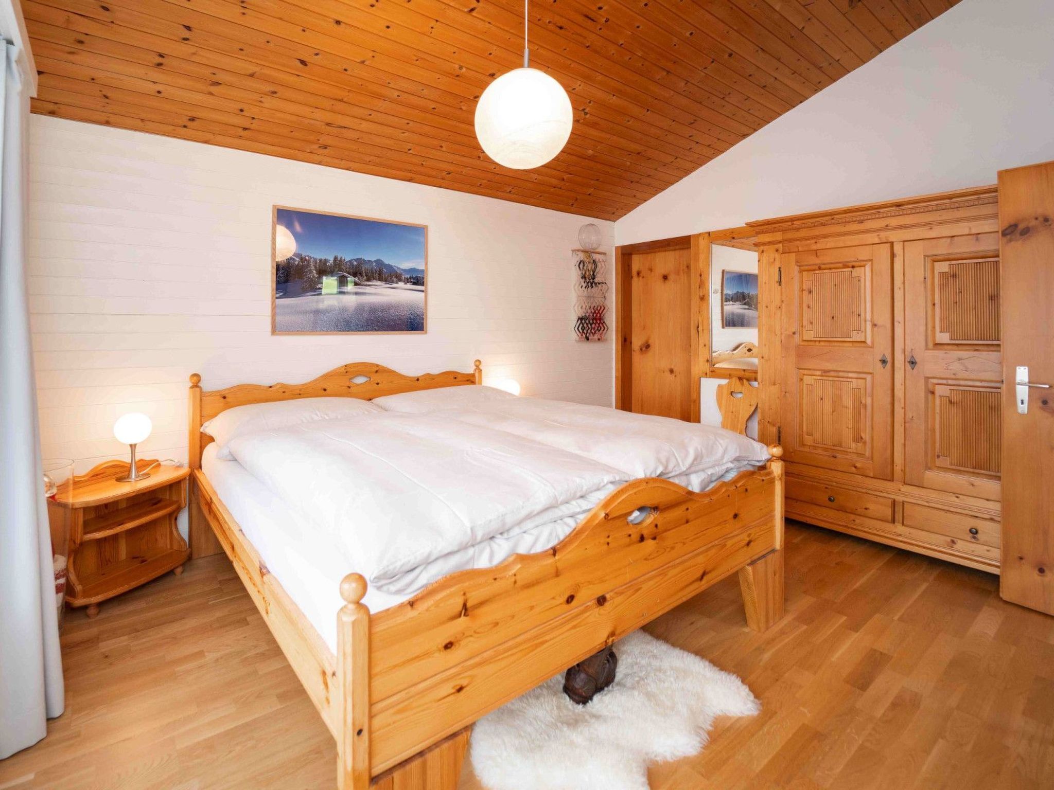 Een houten bed in een kamer met een houten plafond, een aan de muur hangend schilderij en een garderobe.