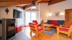 A cozy living room with a fireplace, wooden furniture, and a television. - Arnika Attika, Obersaxen Affeier, (Obersaxen Affeier), 34105B by Interhome (Obersaxen Affeier)