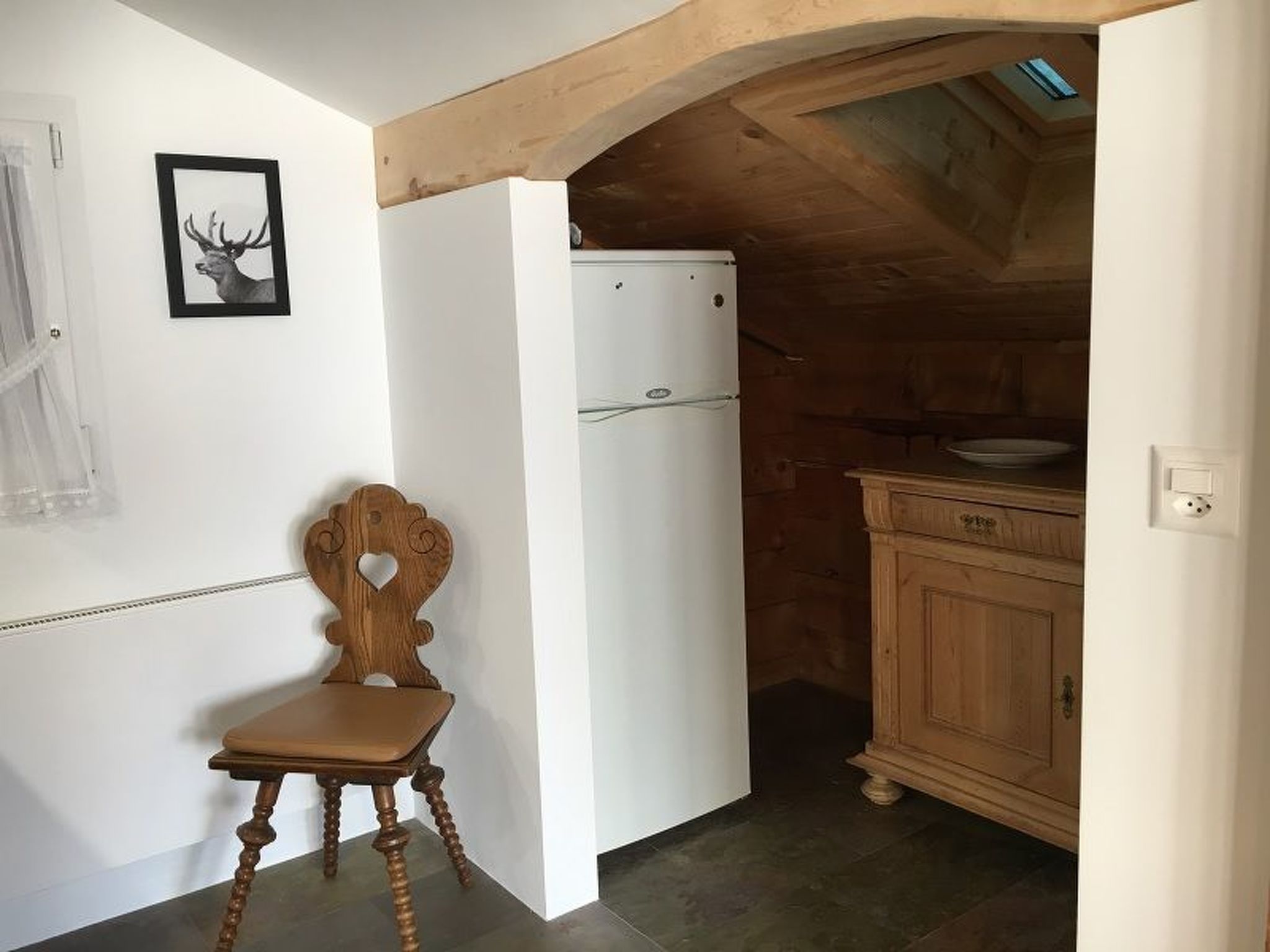 Eine kleine Küche mit einem weißen Kühlschrank, einem Holzkorpus und einem Stuhl mit herzförmiger Lehne.