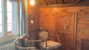 Tunnelmallinen huone, jossa on puuseinä, patteri, kaksi tuolia, kukka-aiheella koristeltu ovi ja riippuvalaisin.