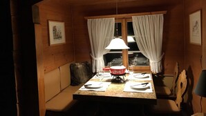 Puisesta ruokailuhuoneesta löytyy pöytä, joka on katettu kahdelle, penkki, riippuvalaisin ja ikkunoissa olevat verhot.