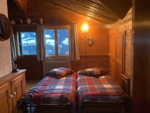 A cozy room with two beds, a window with a view of a snowy landscape, and a wall-mounted light. - Casa Vesta Magnifica, Brigels, (Breil/Brigels), 65063B by Interhome (Breil/Brigels)