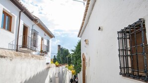 Una calle estrecha con edificios blancos, una reja metálica y una persona caminando.