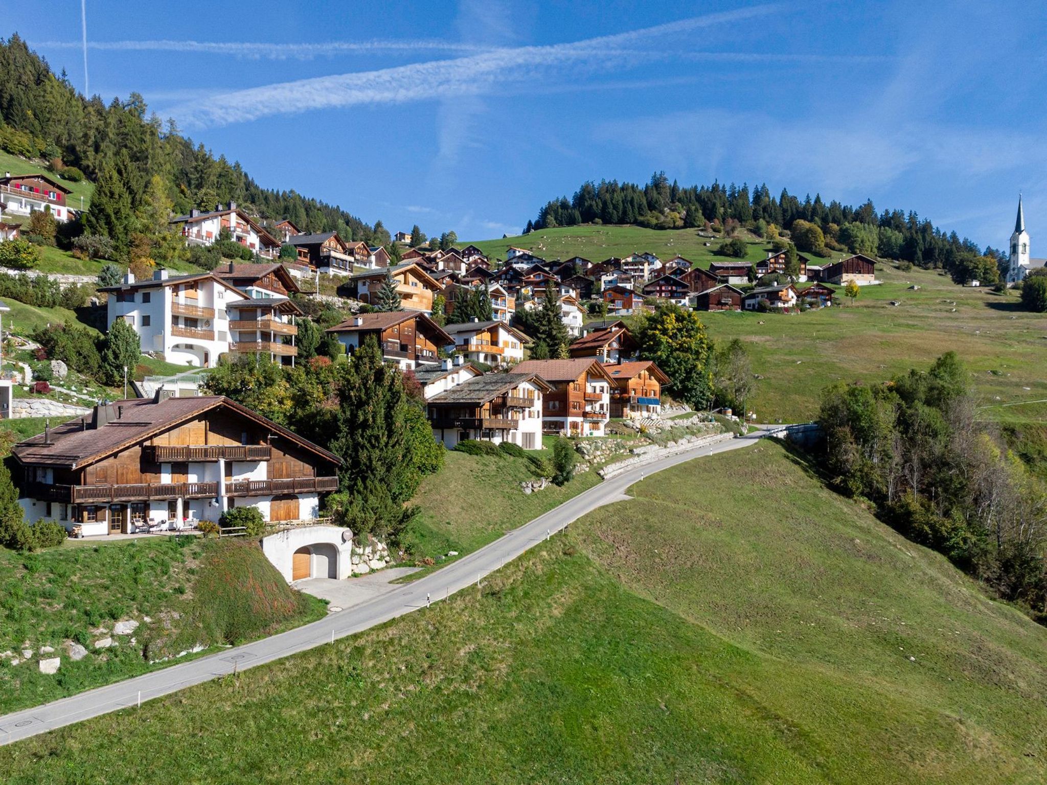 Ein Bergdorf mit traditionellen Chalets, einer kurvenreichen Straße und einem Kirchturm in der Ferne.