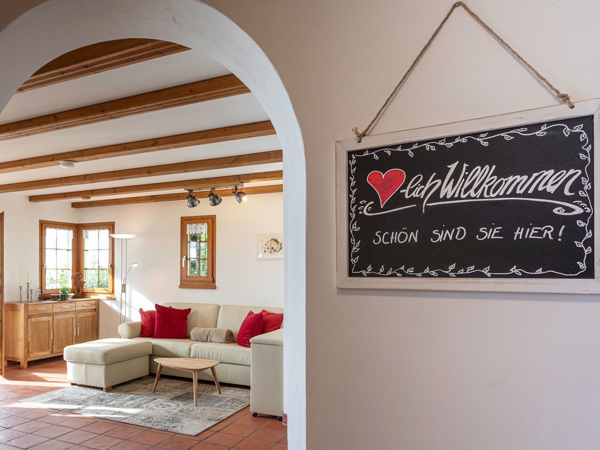 Ein gemütliches Wohnzimmer mit einem Ecksofa, einem kleinen Tisch und einem Kreidetafel-Schild mit einer Willkommensbotschaft.