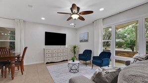 Ein Wohnzimmer mit Deckenventilator, Flachbildfernseher, Esstisch mit Stühlen, einer Couch und einem Couchtisch.