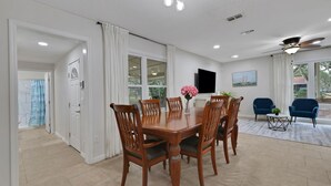 Ein Essbereich mit Holztisch und Stühlen, einem an der Wand befestigten Fernseher und einem Deckenventilator.
