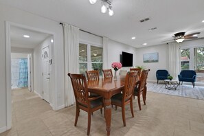 A dining area with a wooden table and chairs, a TV mounted on the wall, and a ceiling fan.