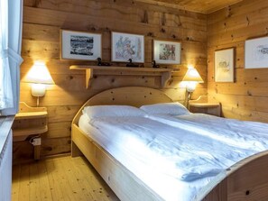 Ein Zimmer mit Holzboden, einem Bett, zwei Nachttischlampen und drei gerahmten Bildern an der Wand.