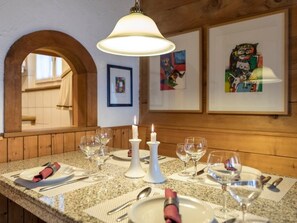 Zona de menjador amb taula preparada per a quatre, un penjó i quadres a la paret.