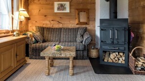 L'interno accogliente di una baita, con un divano, un tavolo con della frutta, un armadietto in legno, un caminetto e una finestra con tende.