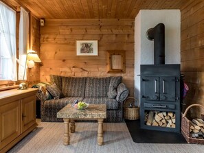 Ein gemütliches Blockhaus-Interieur mit einer Holzcouch, einem kleinen Tisch, einem Kamin und einem Fenster mit Vorhängen.