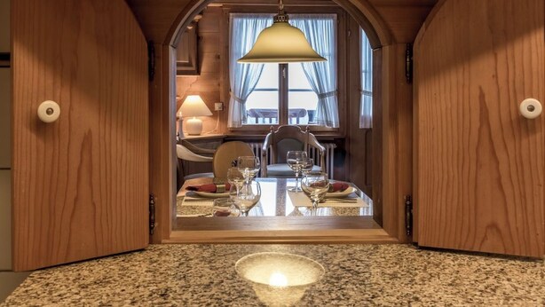 Zona pranzo con un tavolo apparecchiato per due, una lampada a sospensione e rivestimenti in legno.