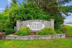 A stone sign with 'BETHANY VILLAGE' and 'PRIVATE BEACH COMMUNITY' text, surrounded by greenery. - Charming Oceanside Getaway! (Bethany Beach)