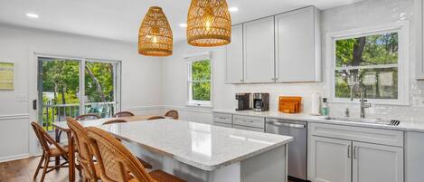 Una cocina moderna con armarios blancos, una isla grande, sillas de mimbre e iluminación colgante.